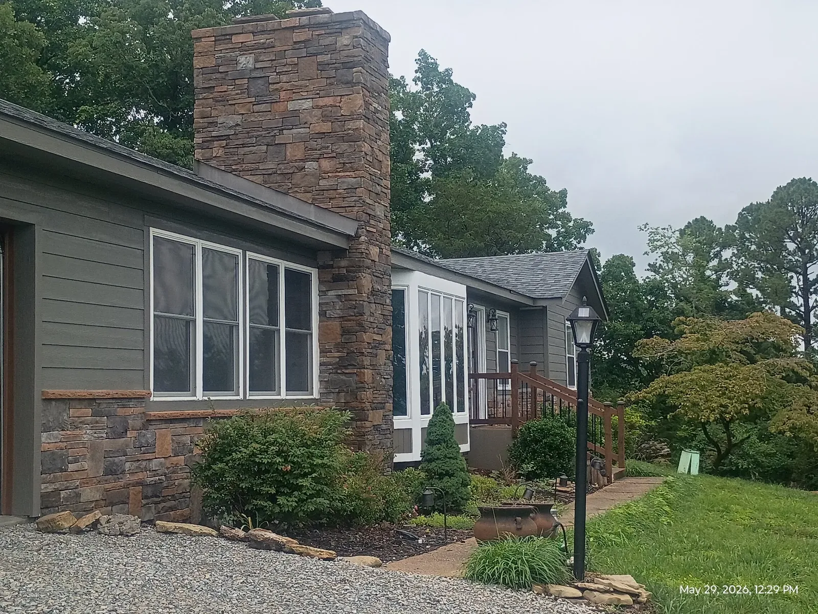 House with a tall stone chimney and matching wainscot seen from a landscaped yard with a lamp post