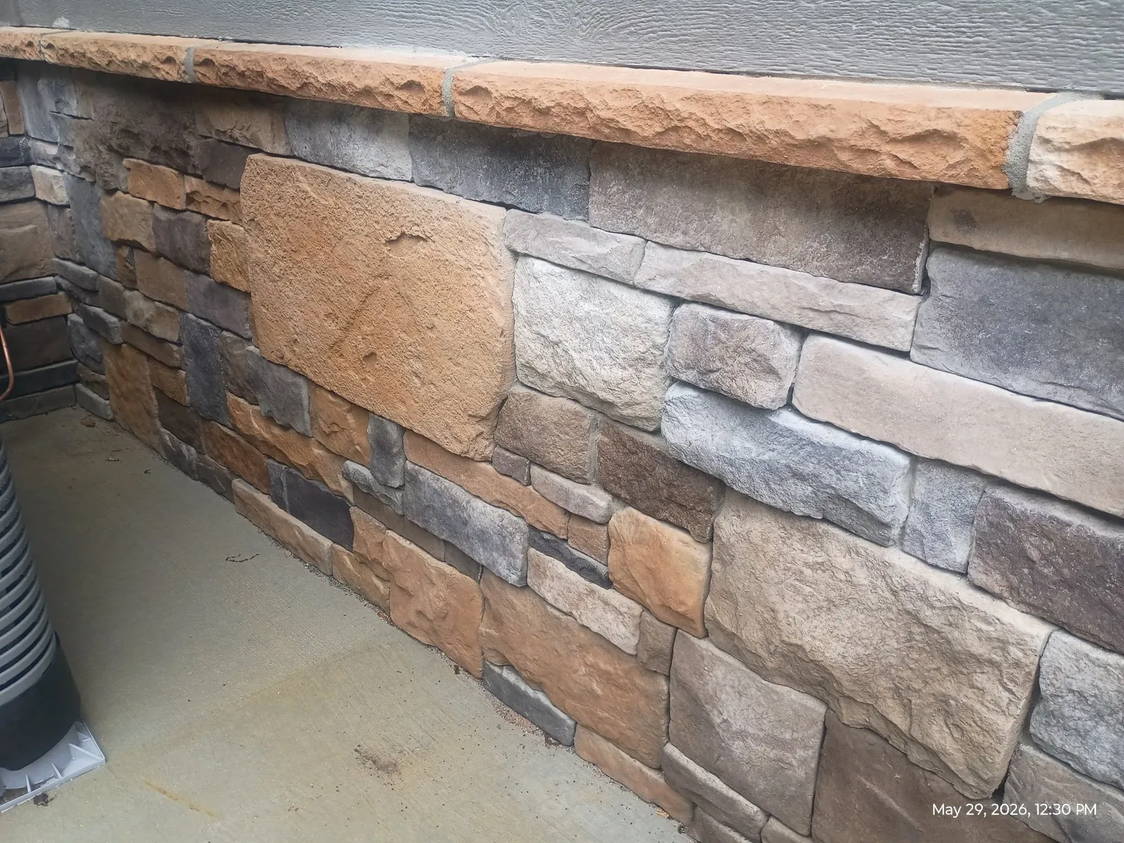 Close-up of a chunky mixed-color stone wall with large pieces under a thick stone cap course