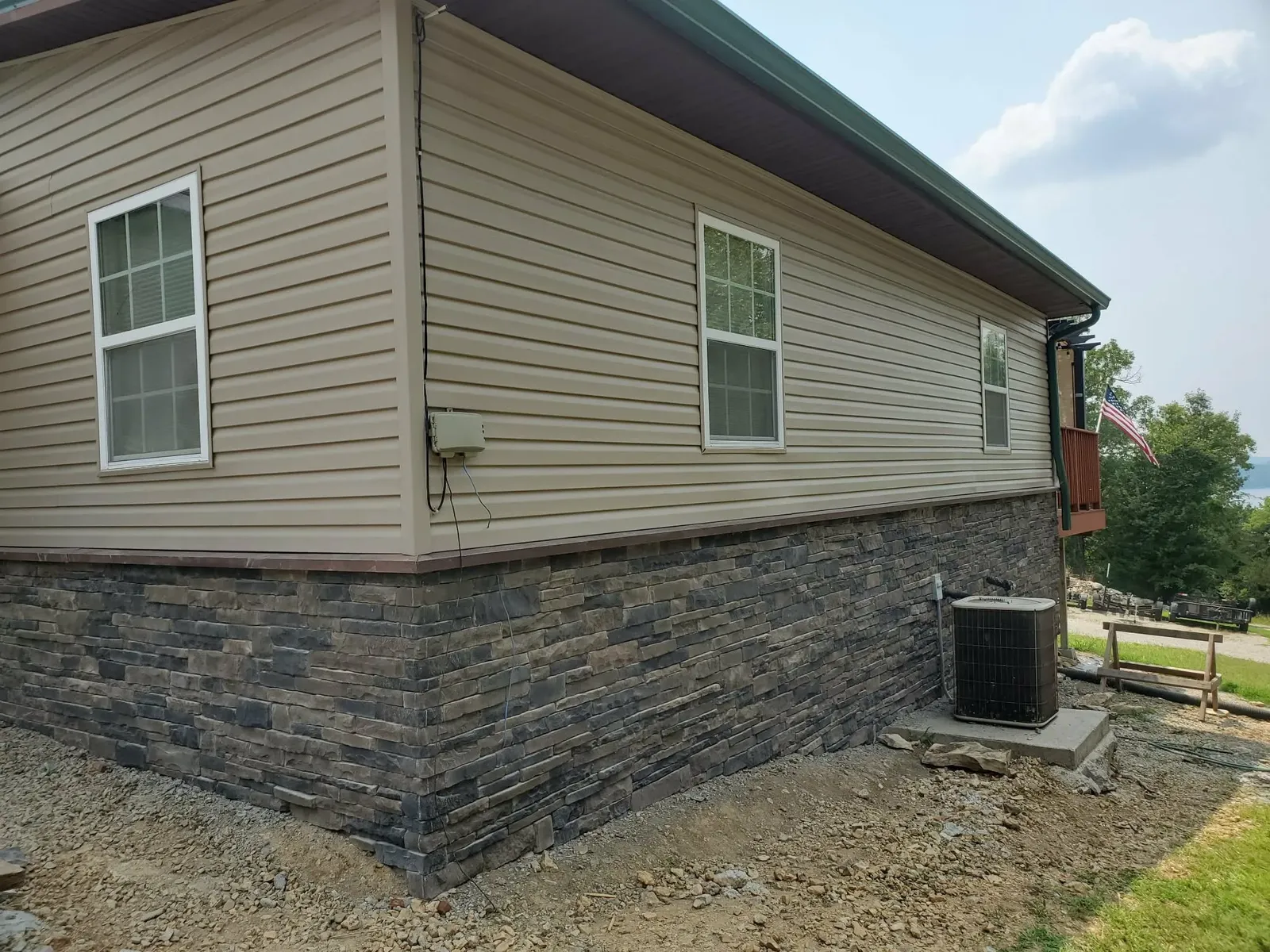 House corner wrapped in dark gray and brown stacked foundation stone, with an air conditioning unit alongside