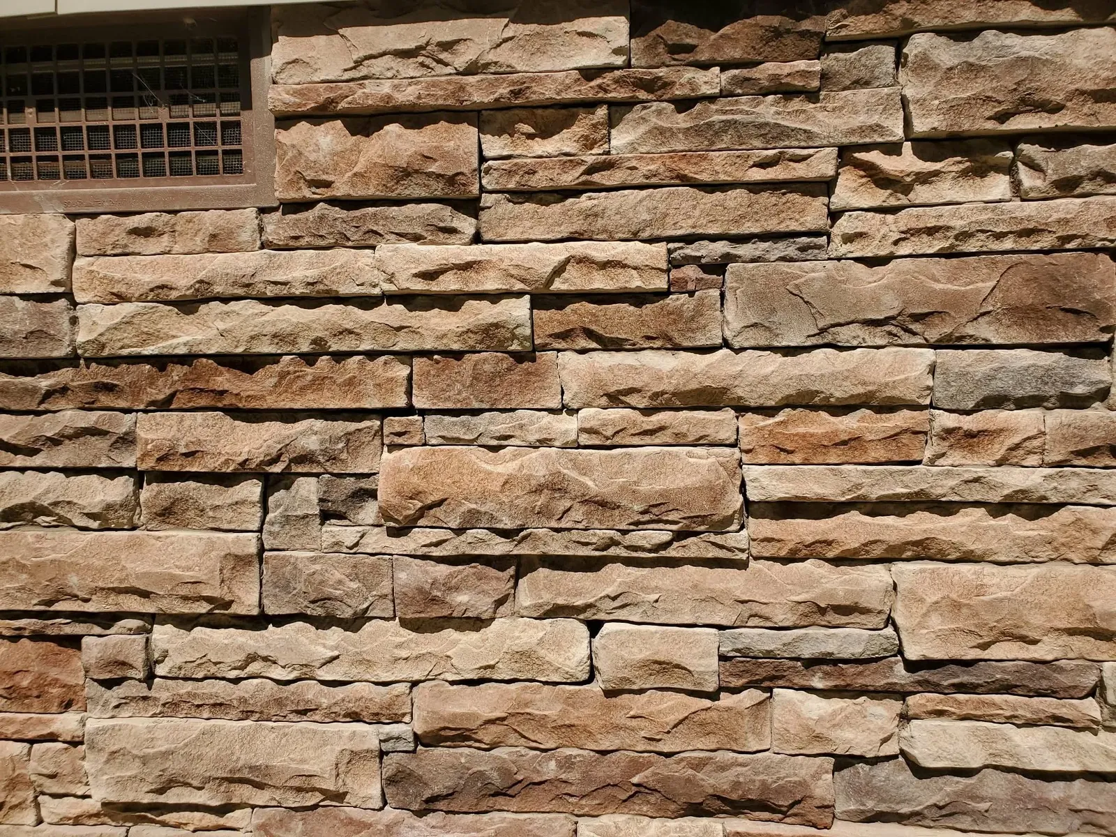 Close-up of warm tan and brown stacked stone with a foundation vent