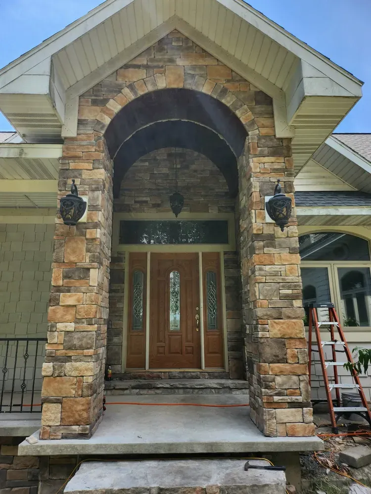 Home entry with arched stone doorway and clad porch pillars