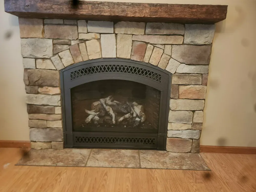 Indoor fireplace with arched stone surround and dark wood mantel