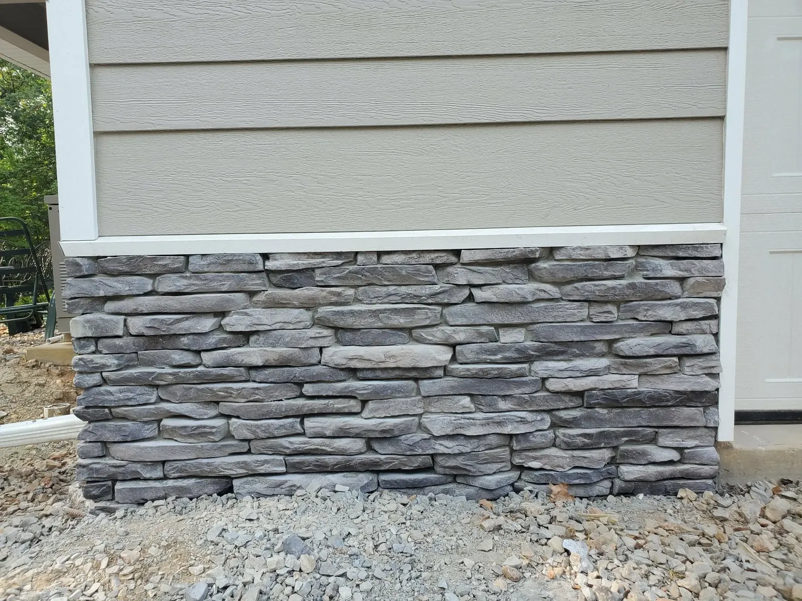 Gray stacked stone wainscot beside a garage door below beige siding