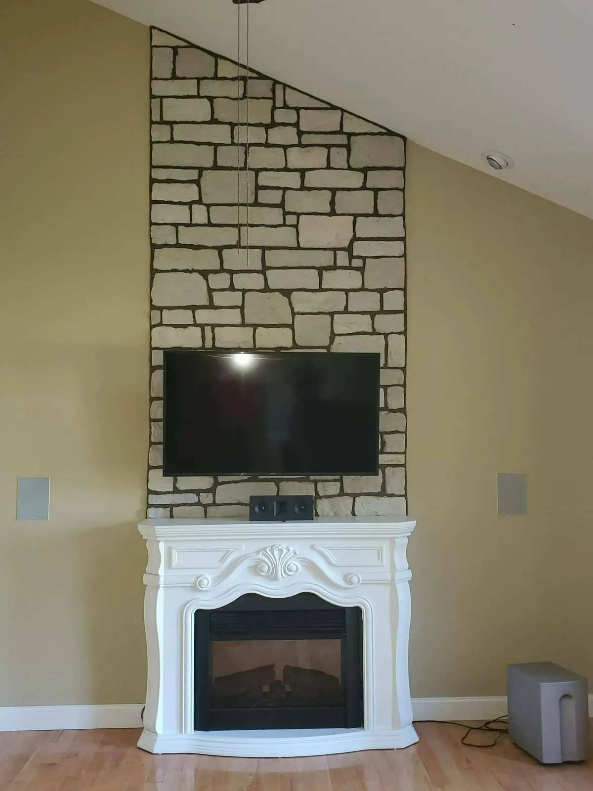 Limestone accent wall rising behind a television above a white decorative fireplace