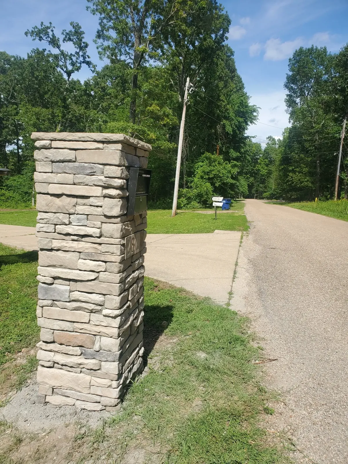 Stone mailbox pillar in light tan and gray stacked stone beside a road, with a cast address number plaque