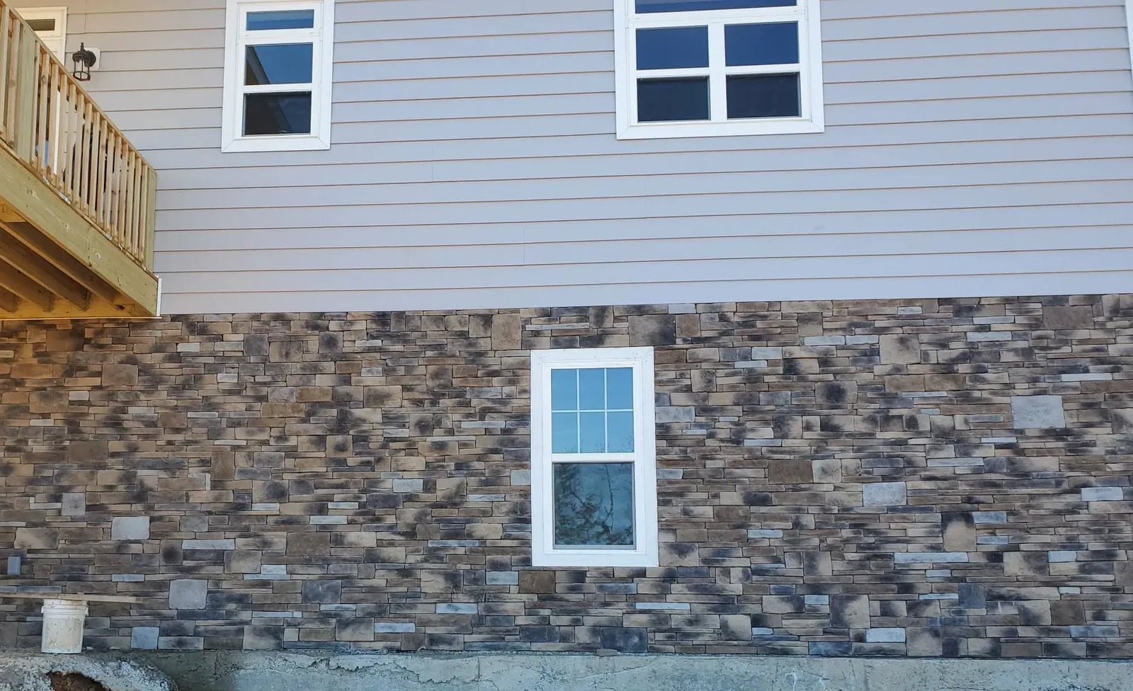 Mottled gray-brown stacked stone foundation wall with a basement window below light siding