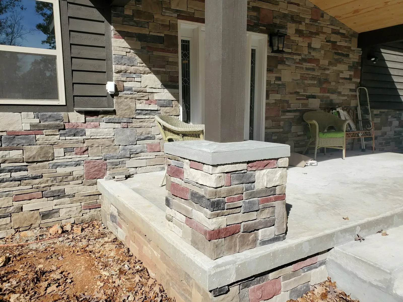 Porch column base in multi-color stone with a flat cap, in front of a stone entry wall