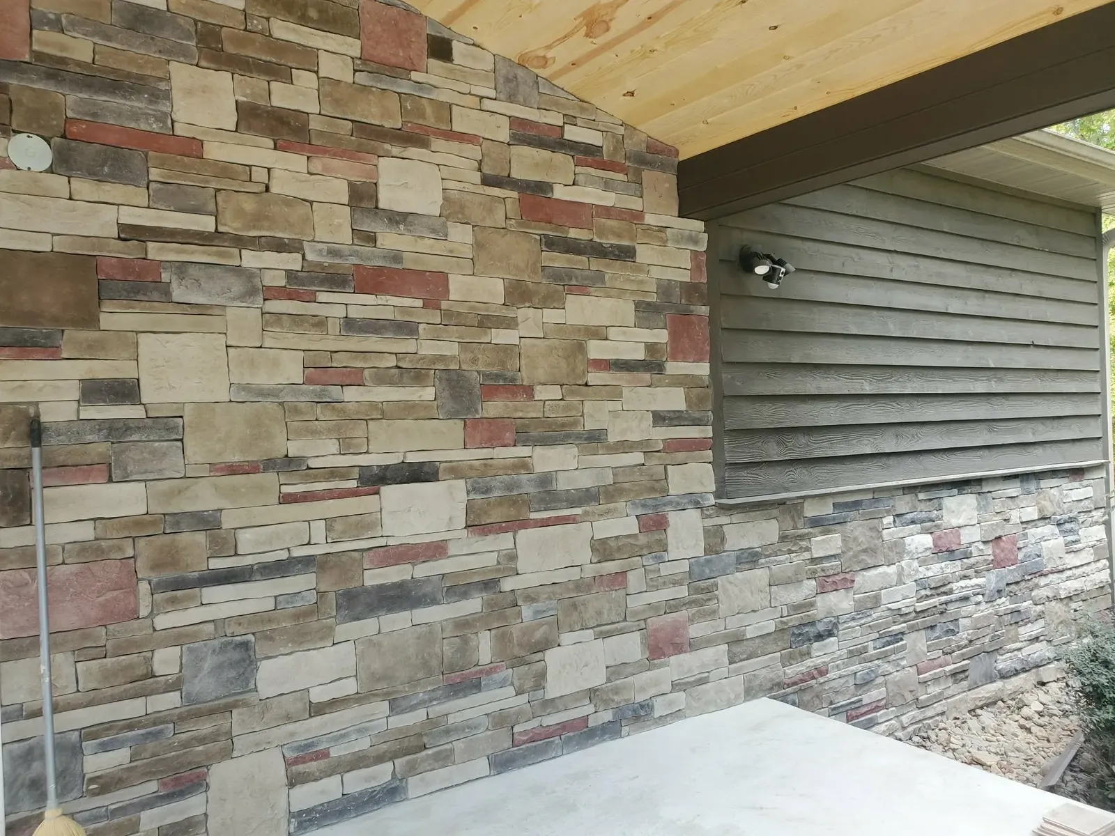 Full-height multi-color stone wall beneath a covered porch, with stone wainscot continuing along the side wall