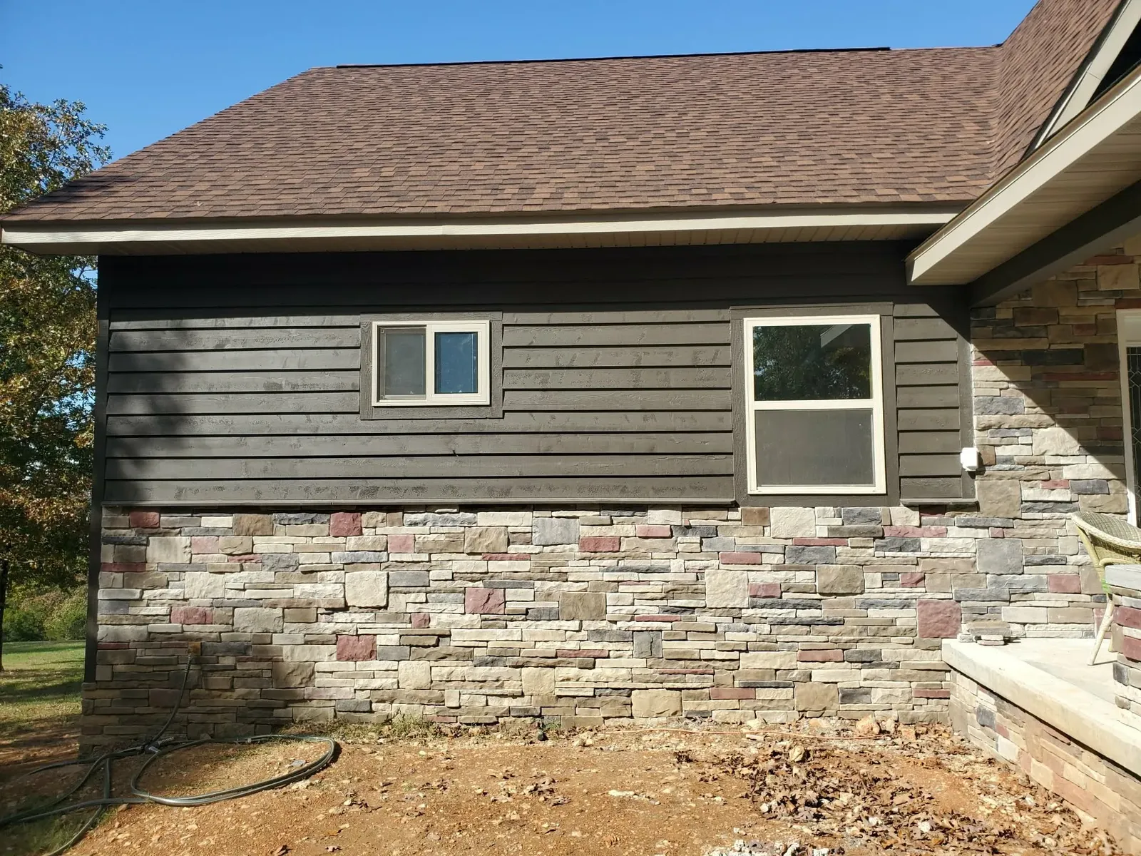 House wall with multi-color stone wainscot with red-toned accent stones below dark siding