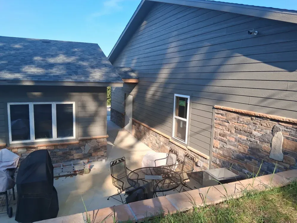 Rear patio of a gray house with stone wainscot and a capped retaining wall