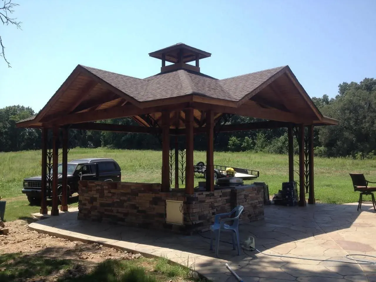 Outdoor pavilion with a stone outdoor-kitchen base on a stamped concrete patio