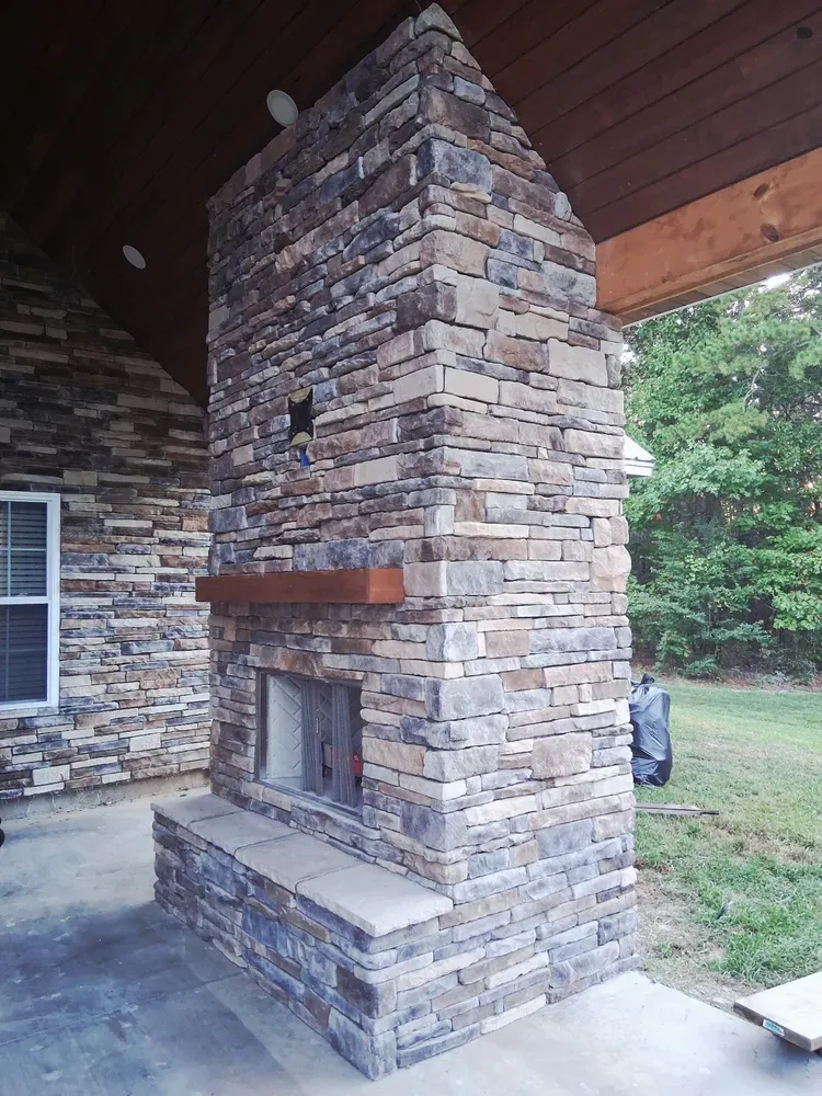 Backyard stone fireplace beside a house wall clad five years earlier in the same matching stone