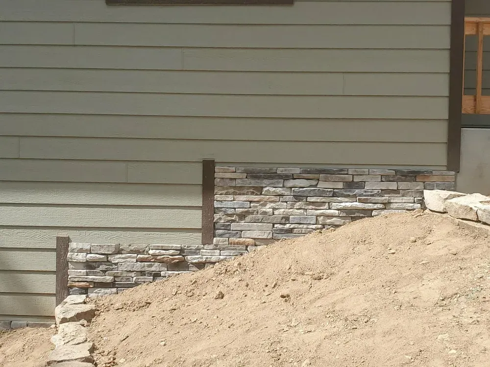 Stone skirting under construction along the base of new-build siding