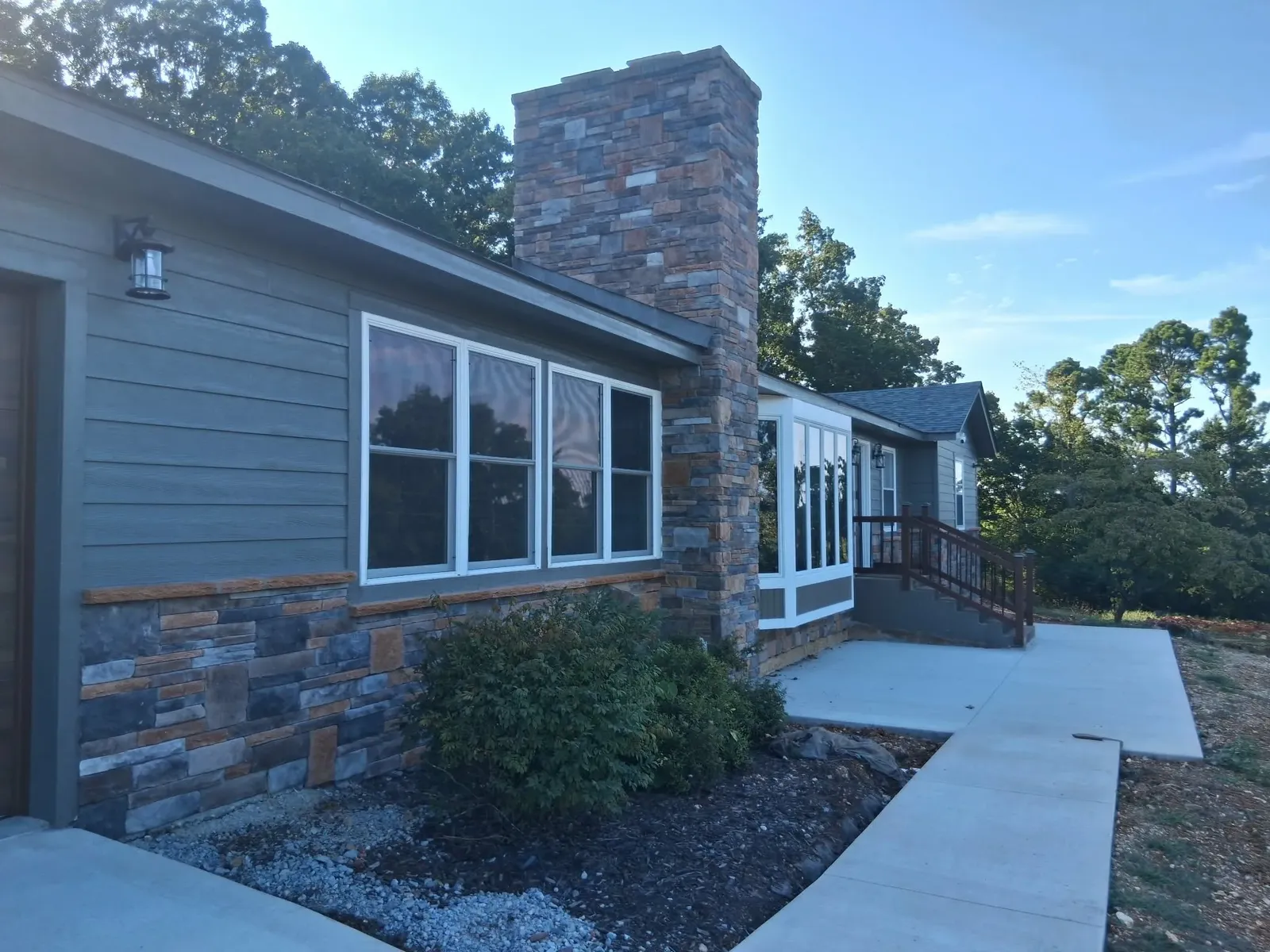 House with a tall full-height stone chimney and matching stone wainscot, a sunroom and a concrete walk