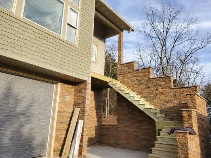 Exterior stone staircase and retaining walls in rusty brown stone beside a garage, work in progress