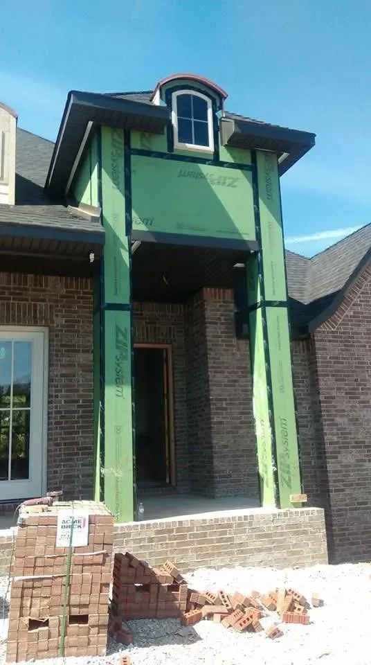 Brick house entry tower still wrapped in green sheathing before the stone work, brick and gravel in the foreground