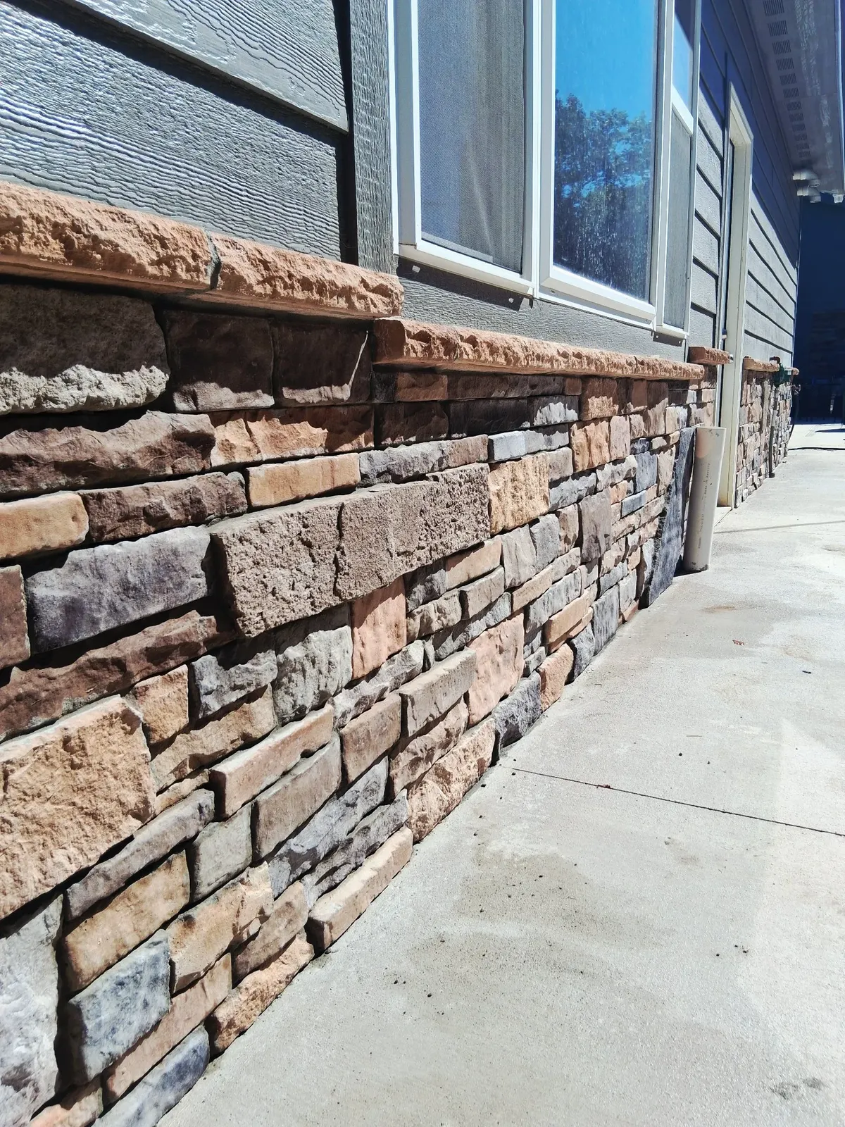 Stone wainscot in warm brown and tan ledge stone with a stone cap course below gray siding