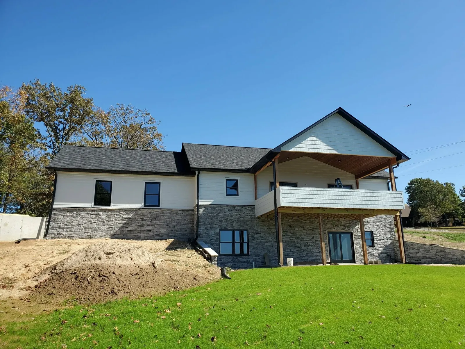 White house with a gray stacked stone lower level and a covered upper deck